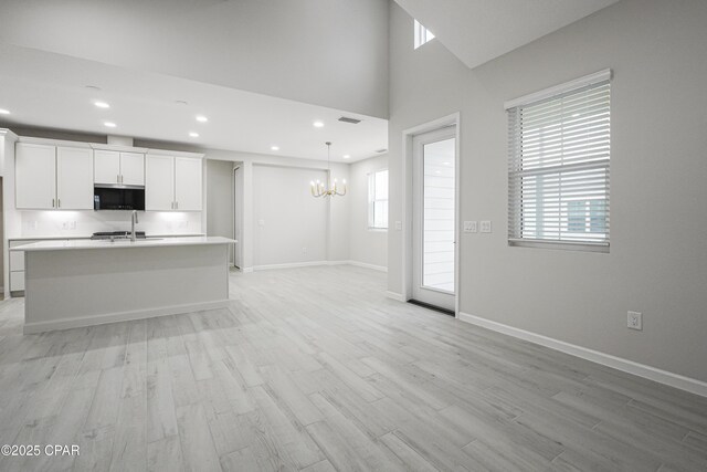 kitchen featuring baseboards, an inviting chandelier, light countertops, a kitchen island with sink, and light wood-style flooring