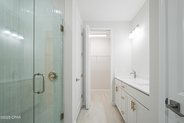 bathroom featuring a stall shower, wood finished floors, vanity, and a spacious closet