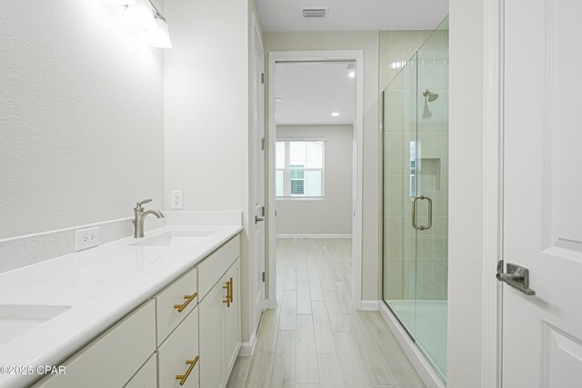full bathroom with double vanity, wood finish floors, a stall shower, visible vents, and a sink