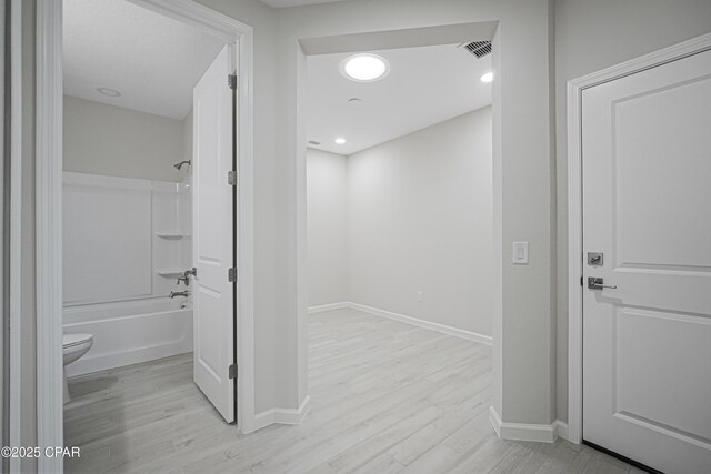 hallway with light wood-style flooring, baseboards, and visible vents