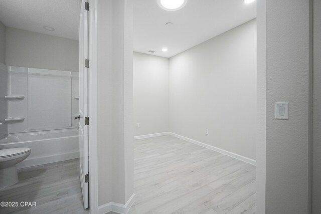 bathroom featuring washtub / shower combination, baseboards, toilet, and wood finished floors