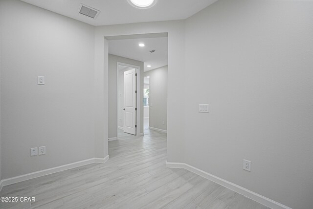 hall with light wood finished floors, visible vents, and baseboards
