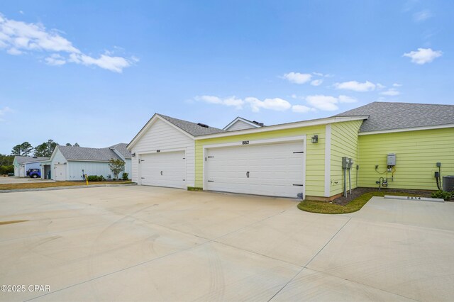 view of front of house with an attached garage, roof with shingles, concrete driveway, and central AC