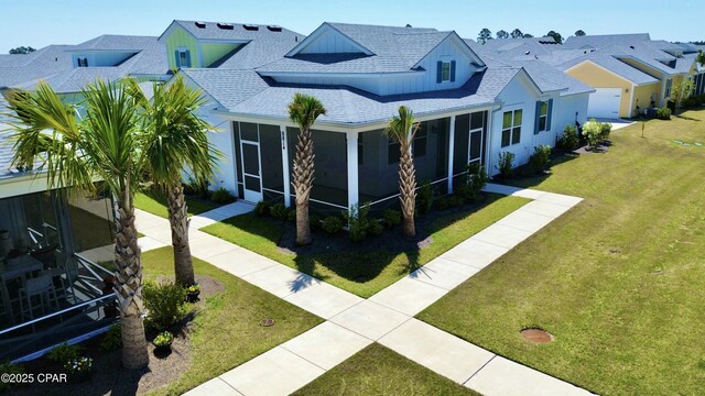 view of front of home with a front yard, a residential view, a sunroom, and a shingled roof