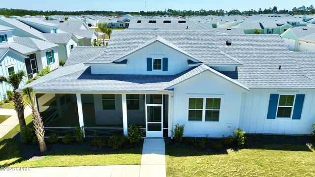 view of front of house with a sunroom, board and batten siding, a front lawn, a residential view, and roof with shingles