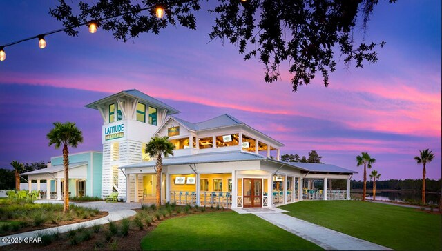 back of property at dusk featuring covered porch and a lawn