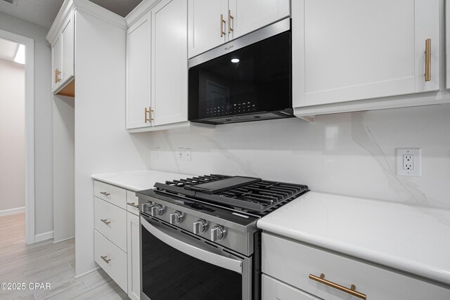 kitchen featuring stainless steel range with gas stovetop, baseboards, light countertops, light wood-style floors, and white cabinetry