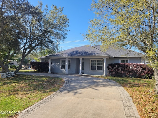 view of front facade featuring roof with shingles, curved driveway, a front lawn, and stucco siding