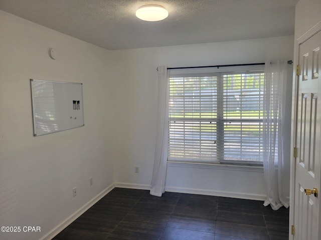 spare room featuring plenty of natural light, dark tile patterned floors, baseboards, and a textured ceiling