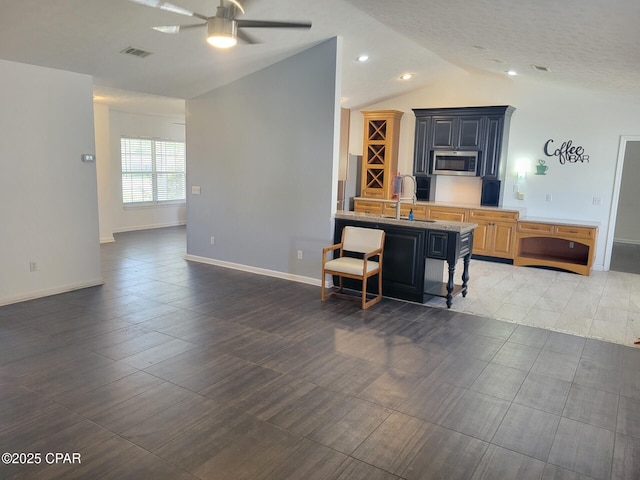 kitchen featuring stainless steel microwave, a breakfast bar, light countertops, a ceiling fan, and a sink