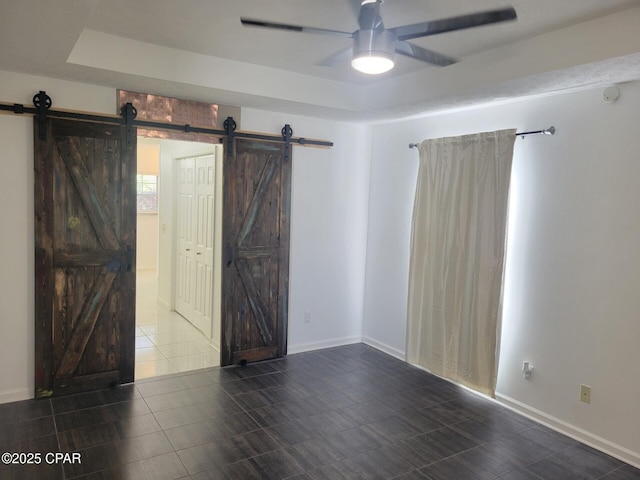 tiled empty room featuring a raised ceiling, a barn door, baseboards, and ceiling fan