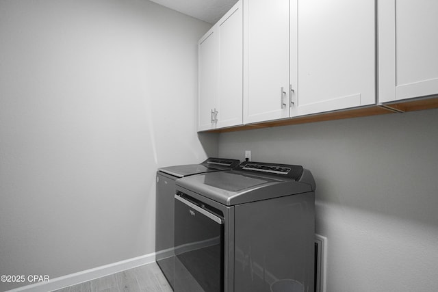 laundry area featuring washing machine and dryer, baseboards, cabinet space, and wood finished floors