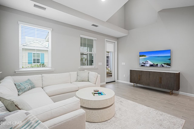 living area with baseboards, visible vents, vaulted ceiling, and light wood finished floors