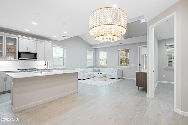 kitchen featuring a sink, a chandelier, glass insert cabinets, light countertops, and stainless steel microwave