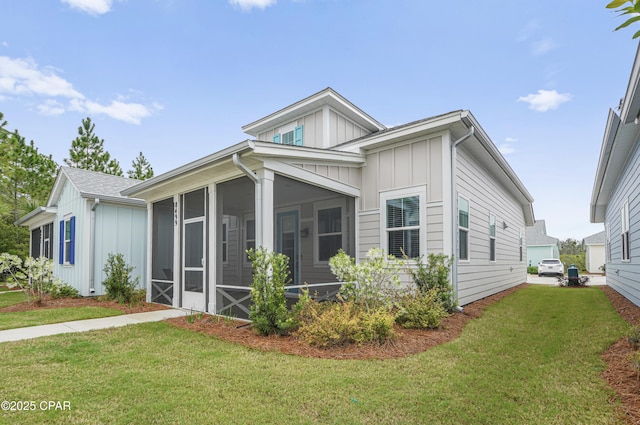 view of side of home with board and batten siding, a lawn, and a sunroom