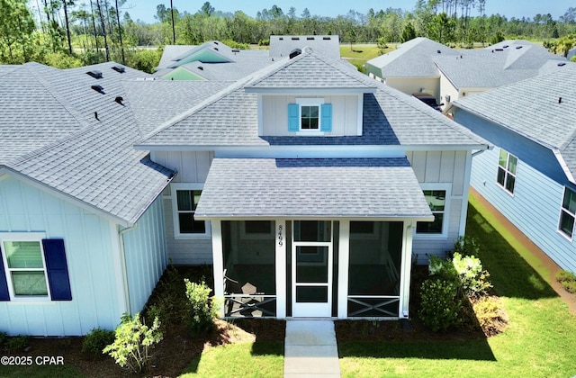 back of house featuring board and batten siding, a sunroom, a yard, and roof with shingles