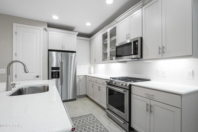 kitchen featuring stainless steel appliances, a sink, recessed lighting, glass insert cabinets, and light countertops