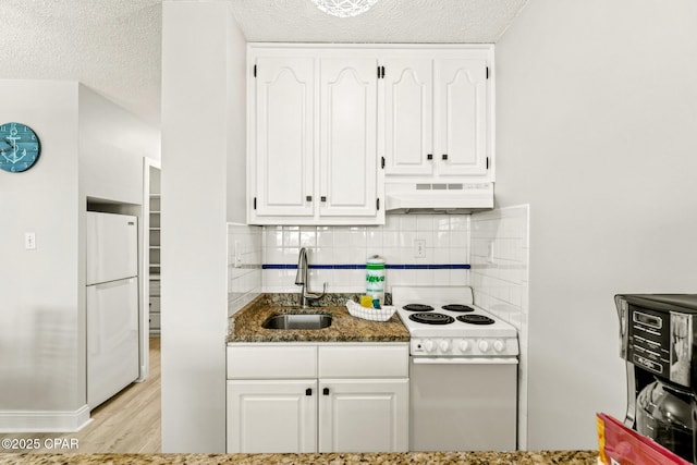 kitchen featuring dark stone counters, white appliances, white cabinets, under cabinet range hood, and a sink