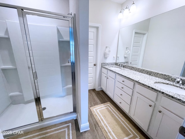 full bath with a sink, a stall shower, double vanity, and wood finished floors