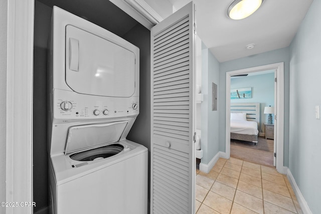 laundry room with stacked washer and clothes dryer, baseboards, and light tile patterned floors