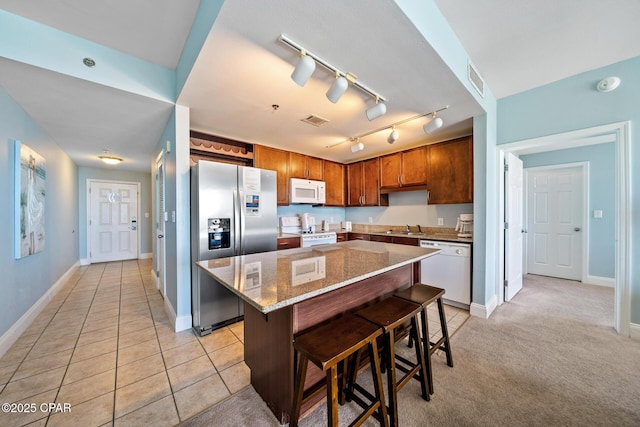 kitchen featuring white appliances, a kitchen bar, a kitchen island, and light stone countertops