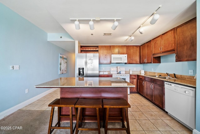 kitchen featuring white appliances, a sink, light tile patterned floors, a kitchen breakfast bar, and a kitchen island