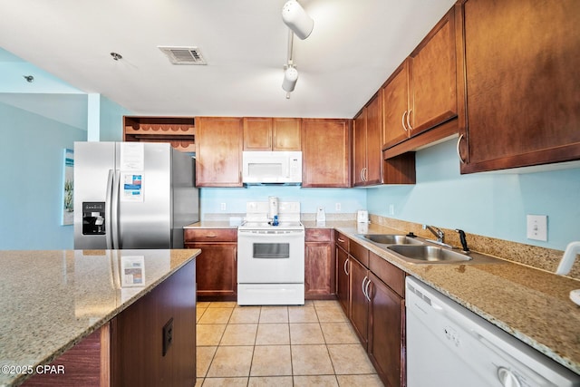 kitchen featuring white appliances, a sink, light tile patterned floors, light stone countertops, and brown cabinetry