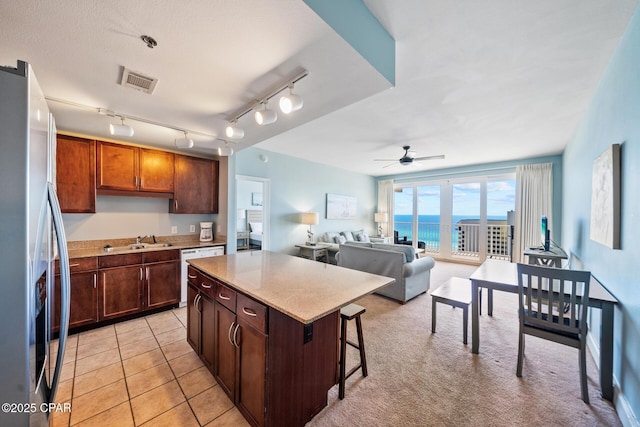 kitchen featuring stainless steel refrigerator with ice dispenser, a sink, a kitchen breakfast bar, a center island, and ceiling fan