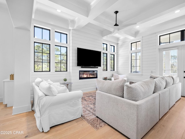 living area featuring light wood-style floors, a fireplace, beam ceiling, and plenty of natural light