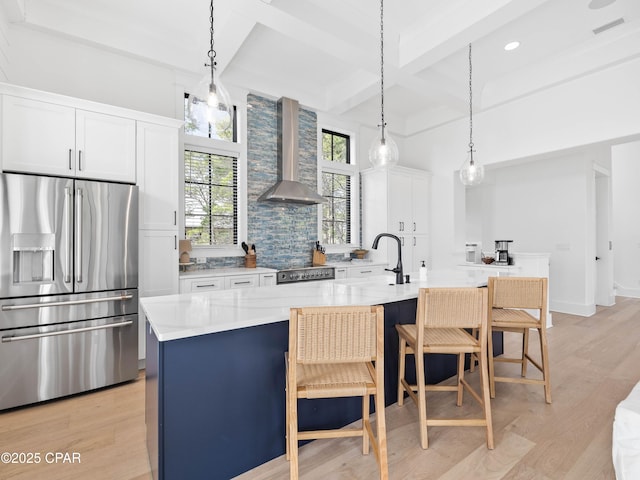 kitchen featuring range, stainless steel fridge, wall chimney exhaust hood, beamed ceiling, and a kitchen bar
