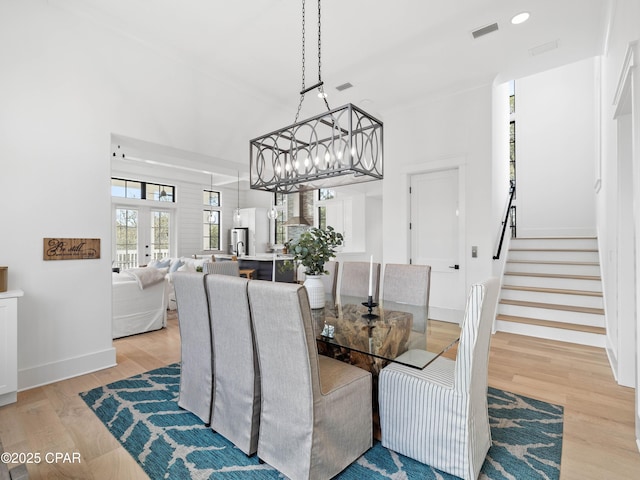 dining area with a notable chandelier, light wood-type flooring, baseboards, stairway, and visible vents