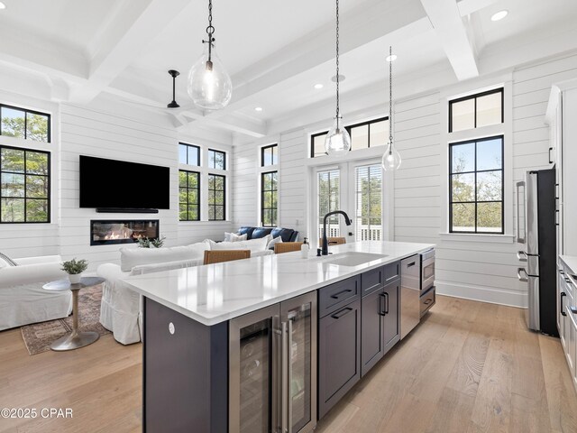kitchen featuring open floor plan, light wood finished floors, a sink, and coffered ceiling