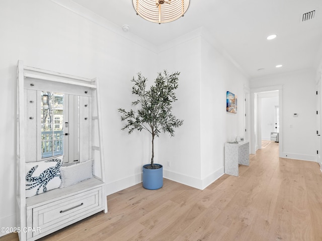 hall featuring light wood-style floors, visible vents, baseboards, and ornamental molding