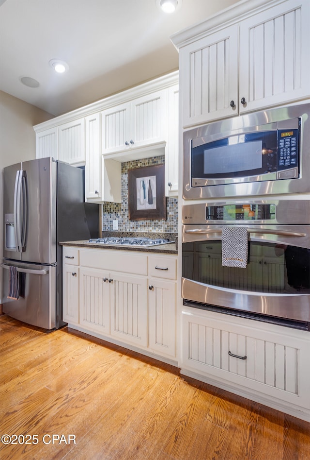 kitchen with decorative backsplash, stainless steel appliances, white cabinets, and light wood-type flooring