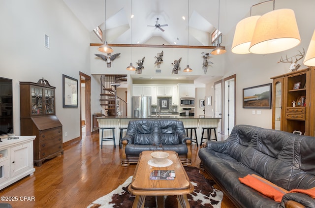 living area featuring visible vents, a ceiling fan, wood finished floors, stairs, and high vaulted ceiling