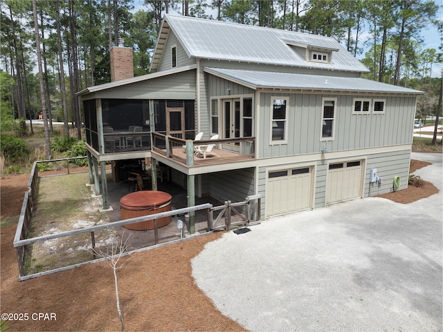exterior space featuring a chimney, metal roof, board and batten siding, a sunroom, and aphalt driveway