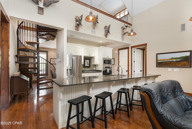 kitchen with dark wood-style floors, stainless steel appliances, a breakfast bar, a sink, and white cabinetry