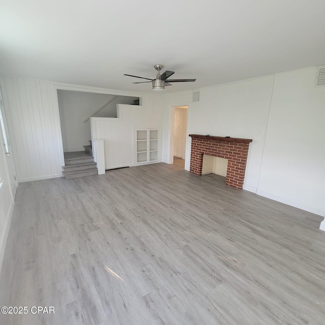 unfurnished living room with stairway, a ceiling fan, wood finished floors, and a fireplace