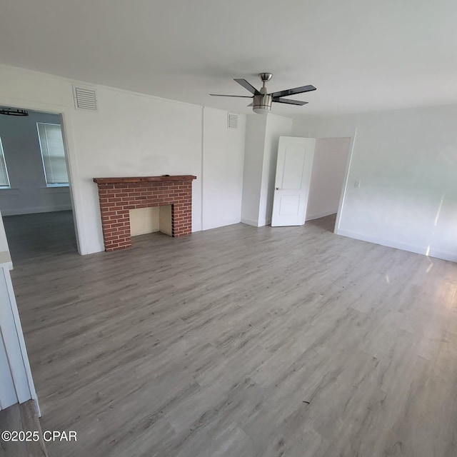 unfurnished living room with a ceiling fan, wood finished floors, visible vents, and a fireplace