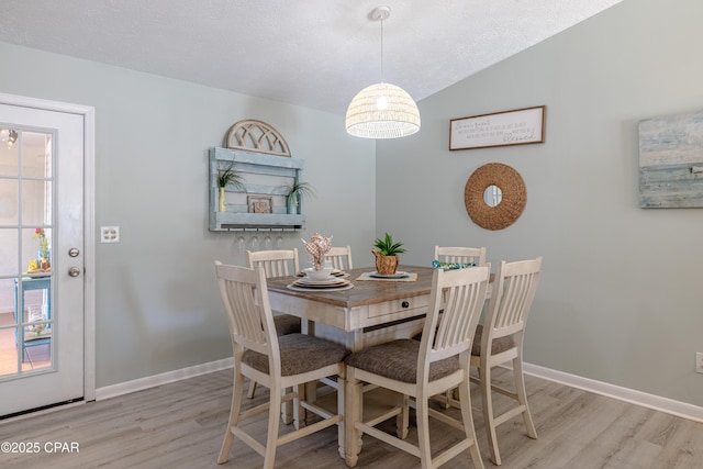 dining room featuring light wood-style flooring, baseboards, a textured ceiling, and lofted ceiling