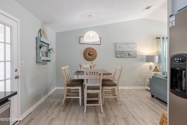 dining area featuring baseboards, light wood-style floors, vaulted ceiling, and a textured ceiling