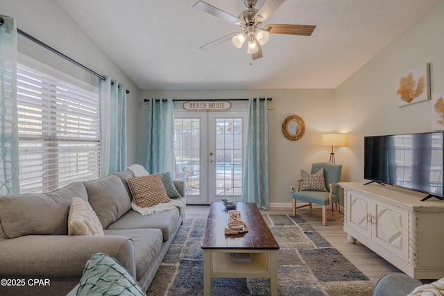 living room featuring light wood-type flooring, french doors, a textured ceiling, lofted ceiling, and ceiling fan