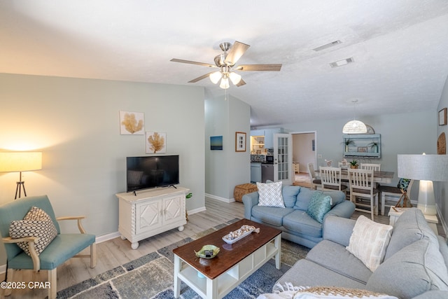 living room featuring a ceiling fan, vaulted ceiling, visible vents, wood finished floors, and baseboards