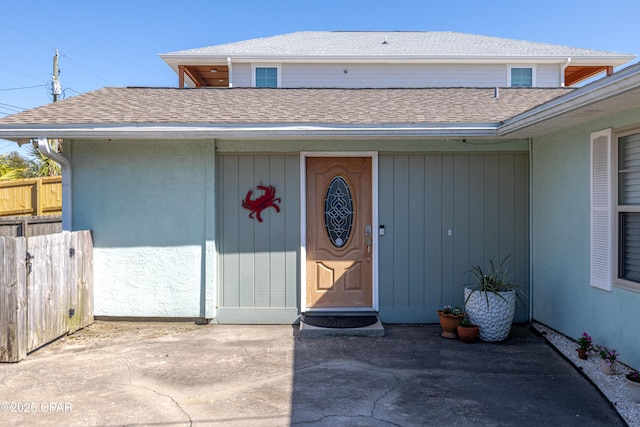 view of exterior entry with roof with shingles and fence