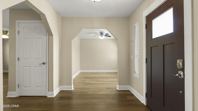 foyer with a ceiling fan, arched walkways, wood finished floors, and baseboards