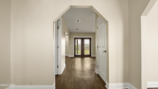 corridor with baseboards, visible vents, arched walkways, and dark wood-style flooring
