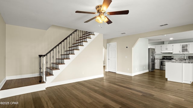 unfurnished living room featuring dark wood finished floors, stairway, baseboards, visible vents, and a ceiling fan