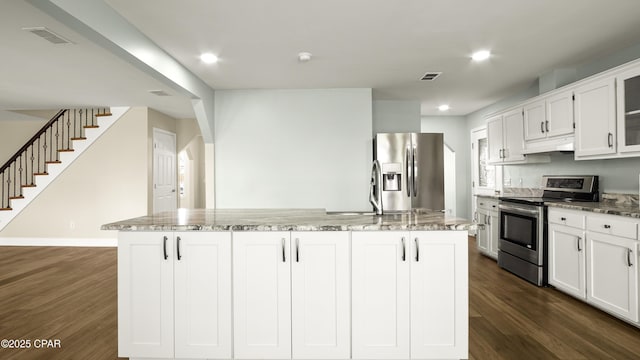 kitchen with light stone counters, stainless steel appliances, under cabinet range hood, dark wood finished floors, and an island with sink