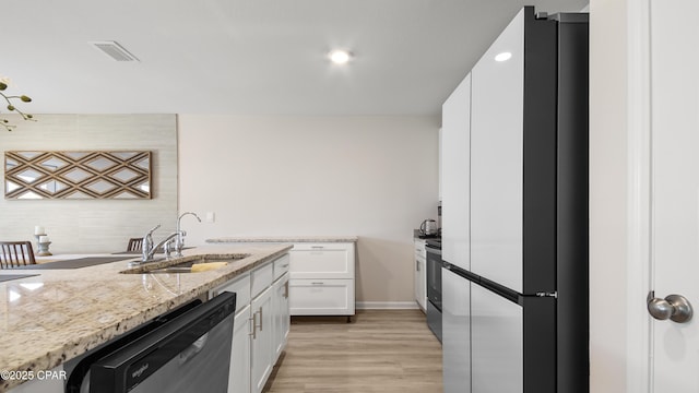 kitchen featuring stainless steel dishwasher, light wood-style floors, white cabinets, light stone counters, and a sink