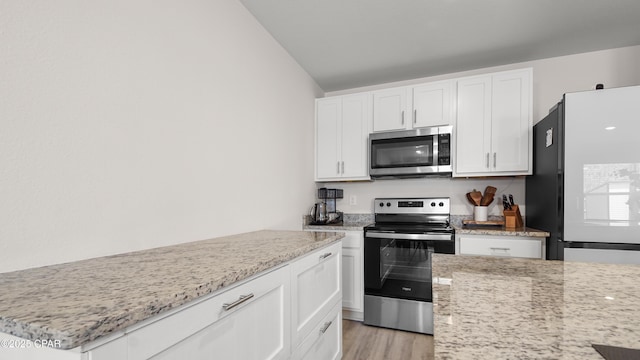 kitchen with white cabinets, stainless steel appliances, light stone counters, and vaulted ceiling